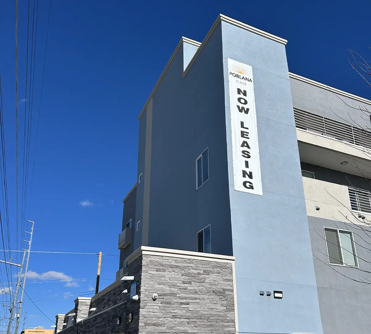 Now Leasing sign on a large greyish blue section of the Poblana Place building.